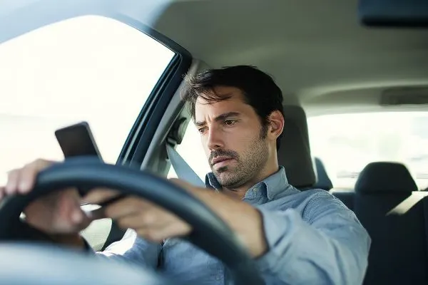 Man driving a car while distracted on his cell phone.