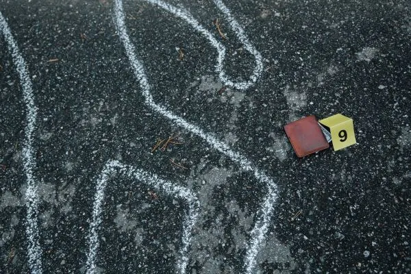 Chalk outline on asphalt next to a wallet and an evidence marker block