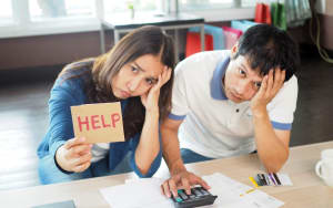 couple holding sign saying help while looking stressed about finances