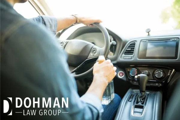 a man in his car driving with a bottle of alcohol in his hand