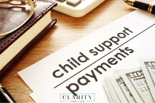 A legal document labeled "child support payments" rests on a wooden desk next to a stack of hundred-dollar bills