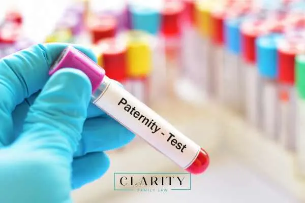 A gloved hand holds a blood sample tube labeled "Paternity - Test" with other tubes in the background.