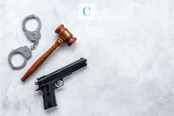handcuffs, a pistol, and gavel in front of a white marbled background