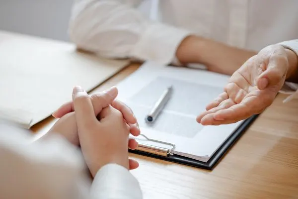 hands on a table with documents and a pen, suggesting a meeting