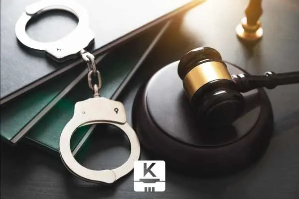 handcuffs rests on top of a stack of books, next to a wooden gavel and sound block on a desk.