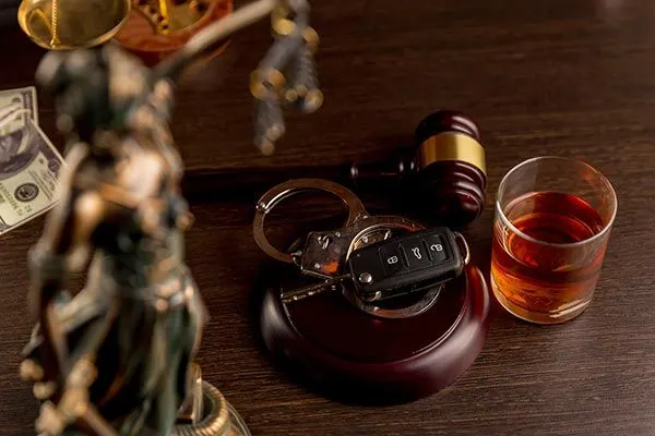 a gavel, handcuffs, a car key, and a glass of whiskey, with a Statue of Justice in the background.