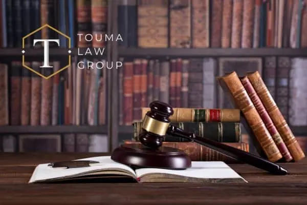 Law books, a gavel, and an open book on a table in front of a bookcase