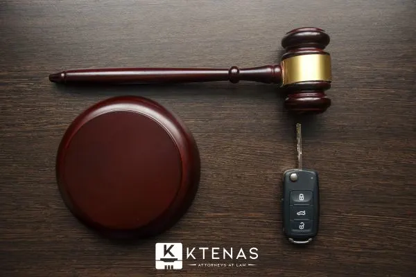 A gavel and its striking block are placed next to a car key fob on a wooden table