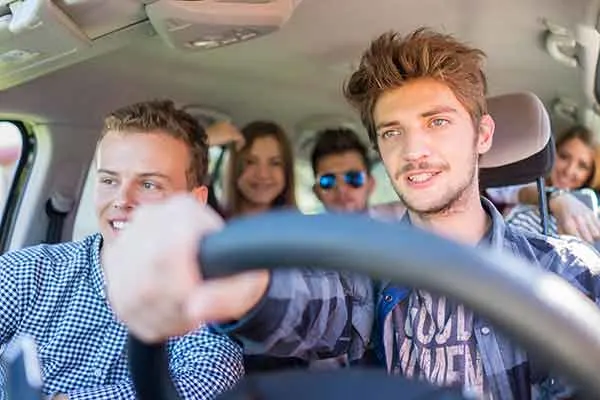 A group of five young friends smiling and laughing while riding together in a car.