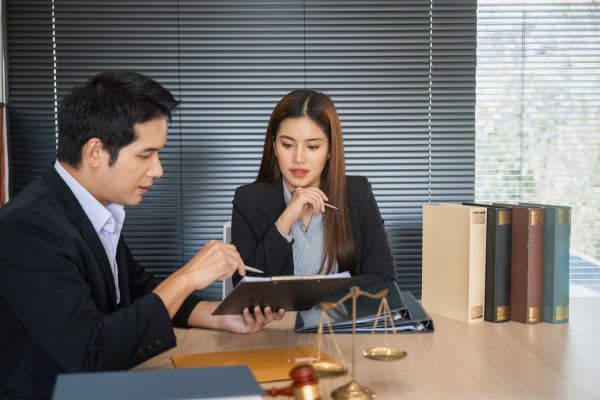 Two professionals, likely legal, review documents at a desk with law books and scales.
