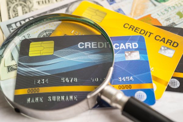A magnifying glass lies on several credit cards and dollar bills