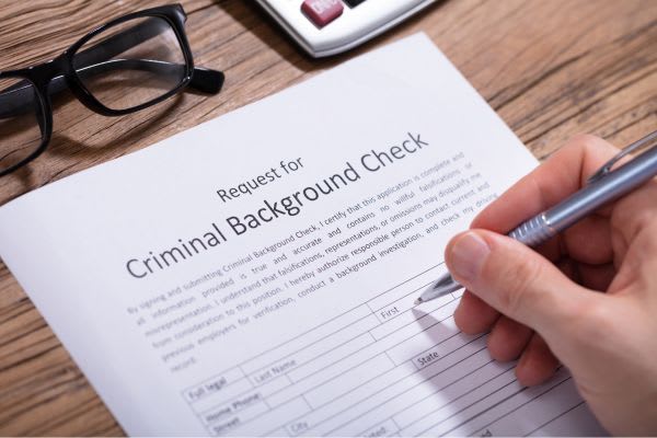 A hand holding a pen filling out a "Request for Criminal Background Check" form.