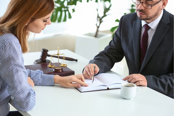 A lawyer points to a document while a client looks on, with a gavel and coffee cup nearby.