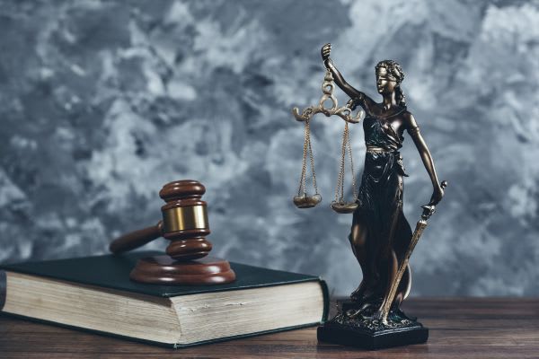 Lady Justice statue standing next to a gavel and a law book.