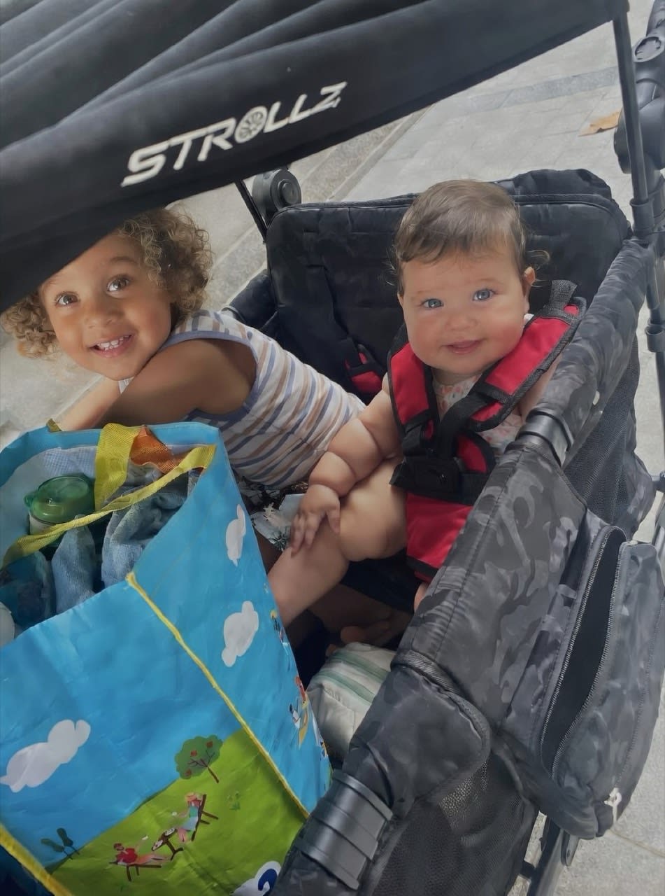 Children sitting in a STROLLZ. stroller wagon with shopping bags during a family outing, highlighting the realities of modern family life.