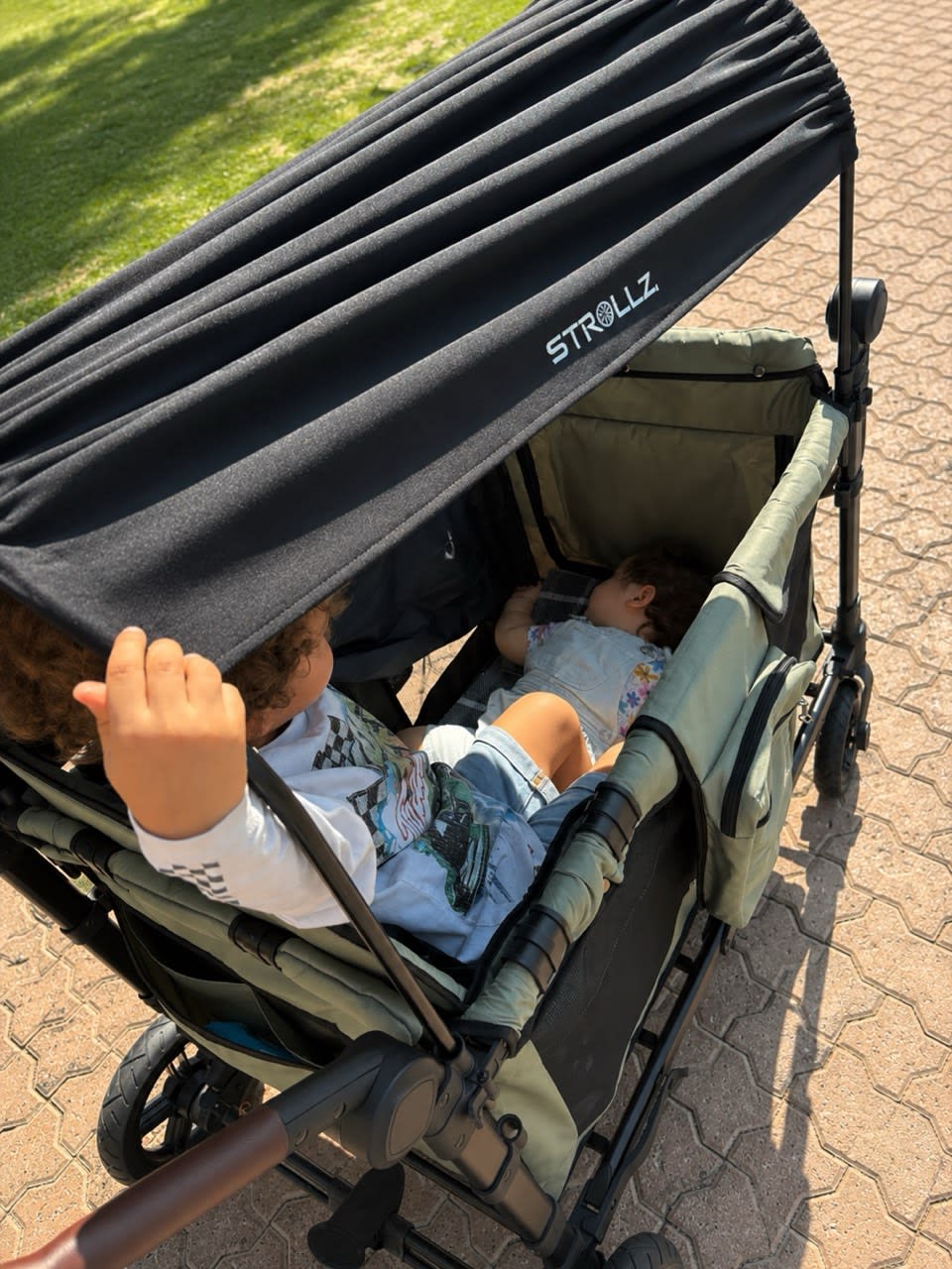 Child resting comfortably under the STROLLZ. canopy while another sibling enjoys the ride.