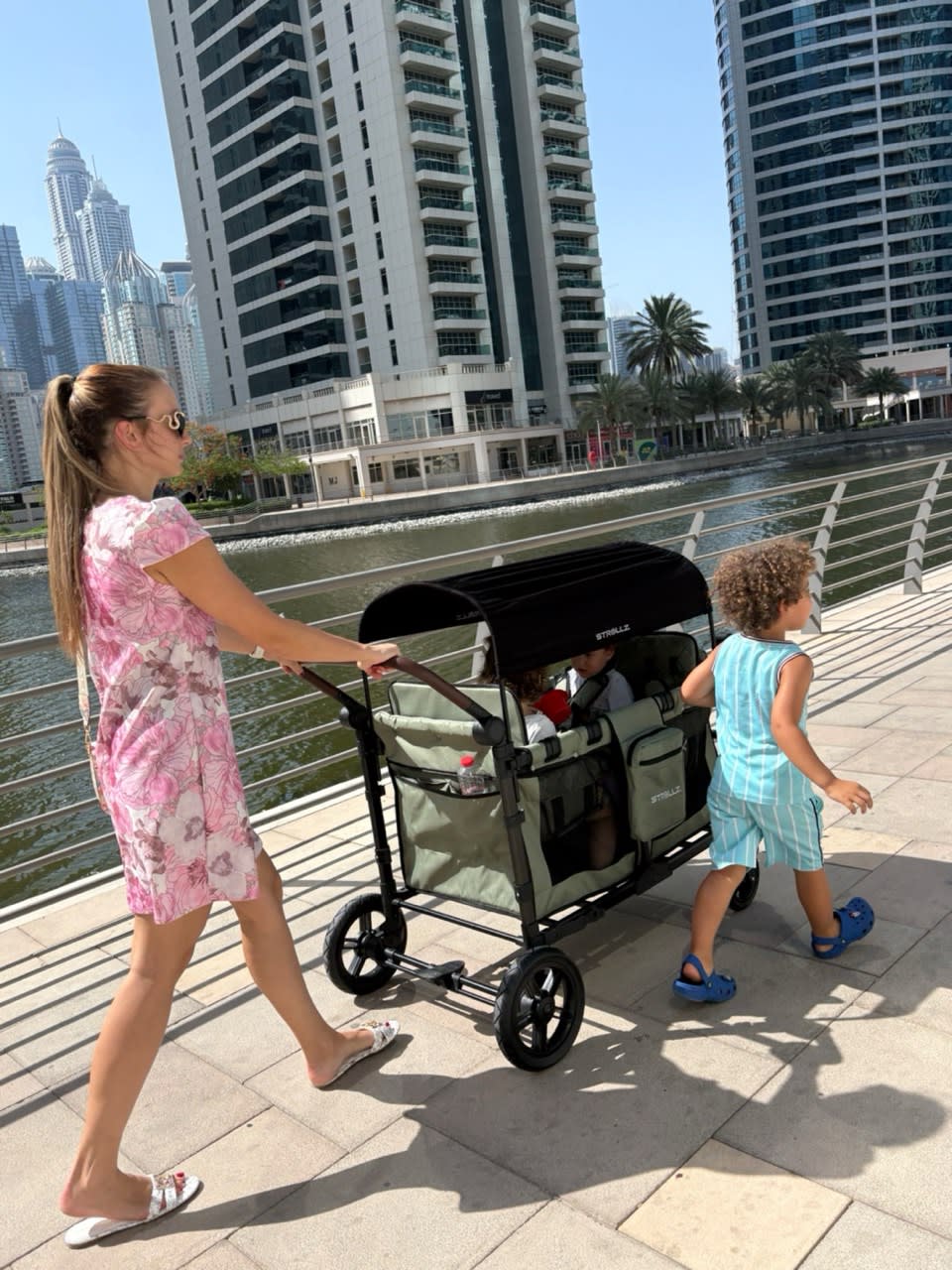 Mother walking with a STROLLZ. stroller wagon while a child walks independently beside it in Dubai Marina.