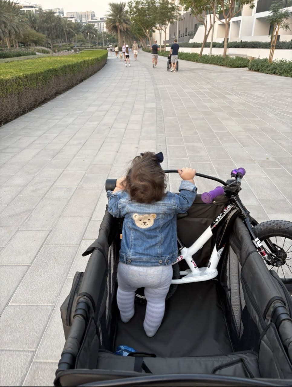 Child standing inside a STROLLZ. stroller wagon with a balance bike during a family walk.