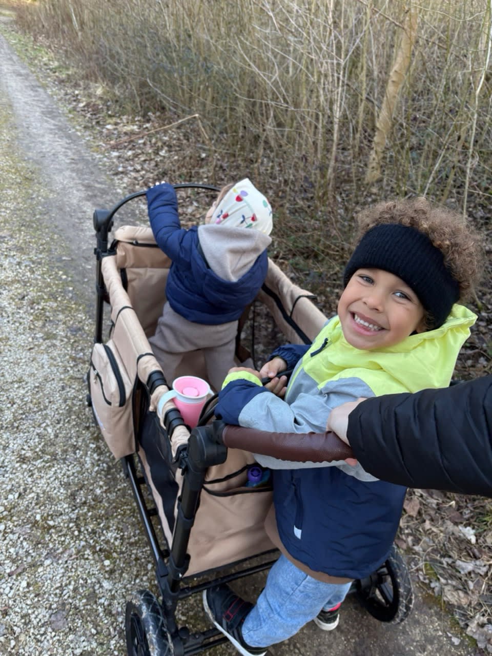 Child walking independently beside a STROLLZ. stroller wagon during a family walk.