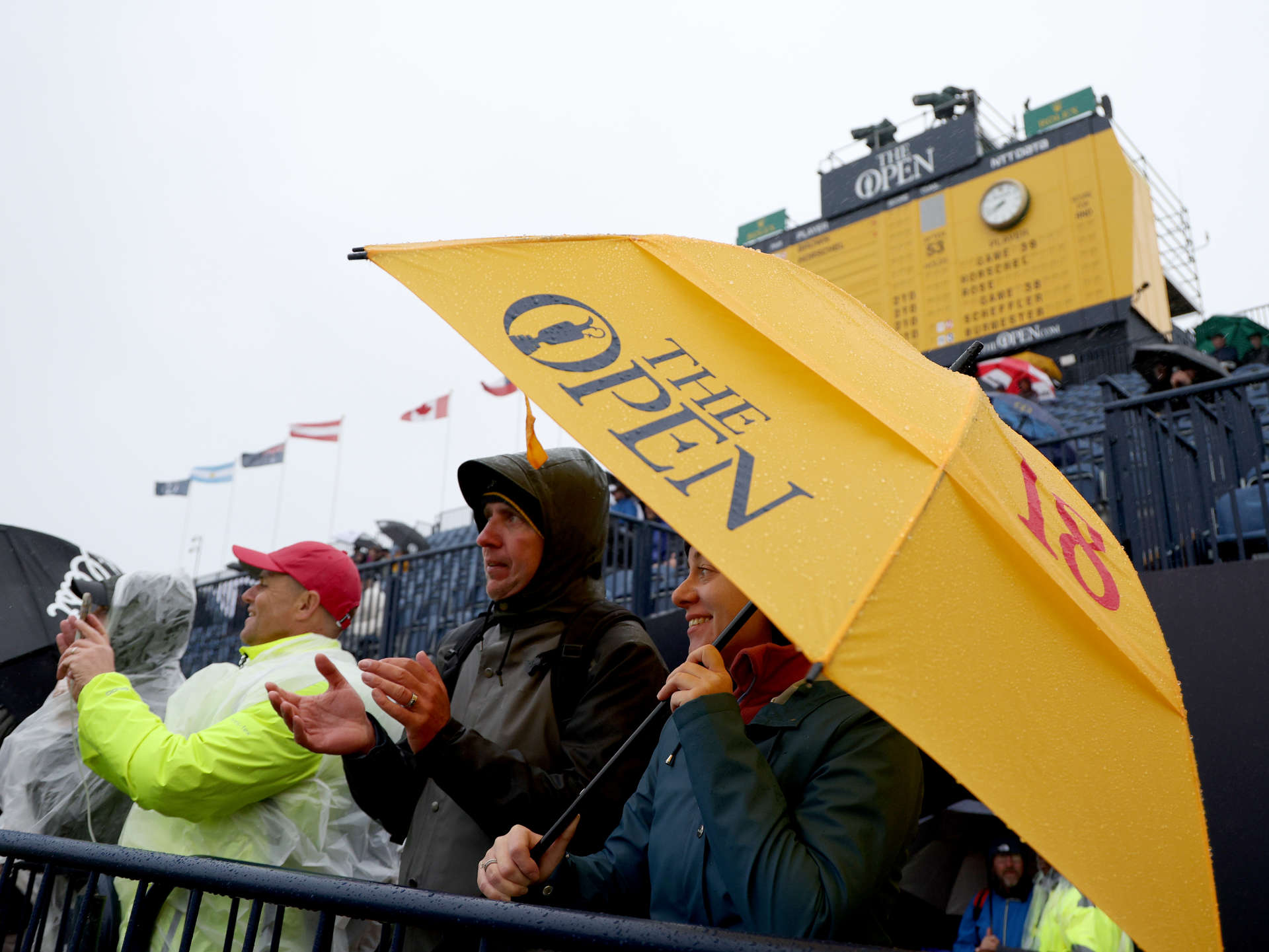 TROON, SCOTLAND - JULY 20: Fans shelter under an umbrella as they watch on at the side of the 18th green during day three of The 152nd Open championship at Royal Troon on July 20, 2024 in Troon, Scotland. (Photo by Harry How/Getty Images)