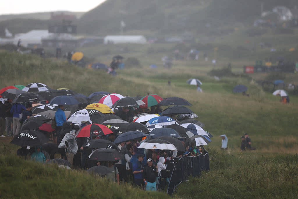 Spectators shelter under umbrellas as the rain falls on day two of the 153rd Open Championship at Royal Portrush golf club in Northern Ireland on July 18, 2025. (Photo by HENRY NICHOLLS / AFP) / RESTRICTED TO EDITORIAL USE (Photo by HENRY NICHOLLS/AFP via Getty Images)