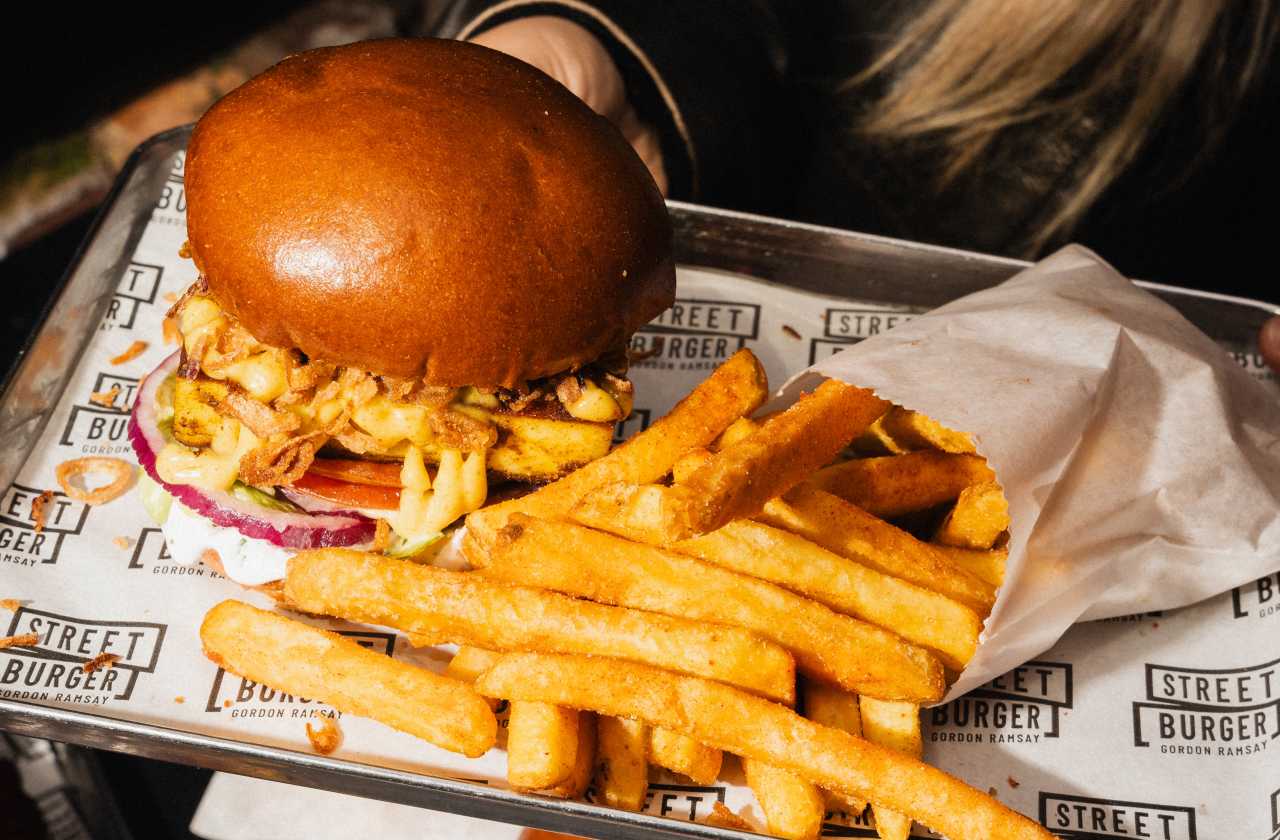 A person holding a tray with a burger and fries on it at Street Burger.