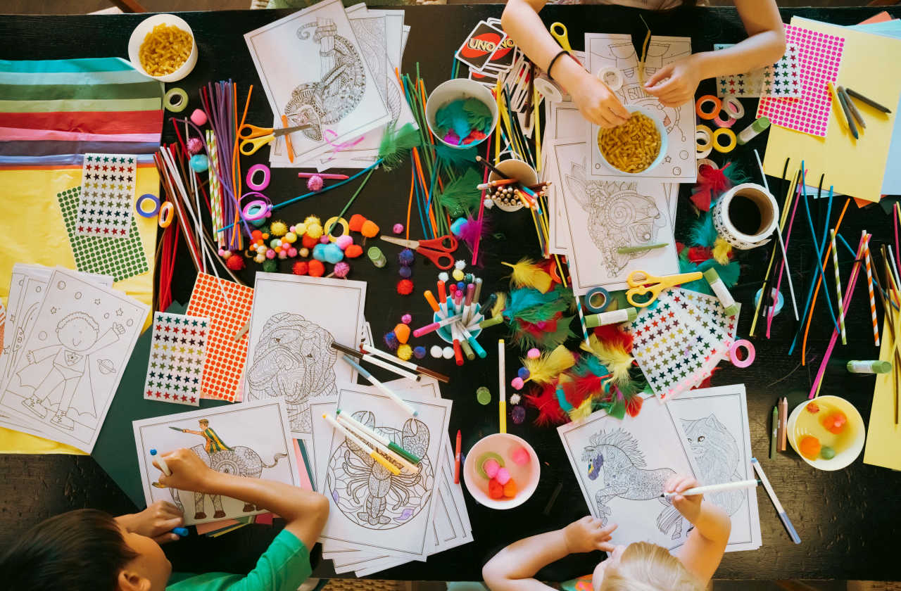 Three children at a craft table drawing and creating.