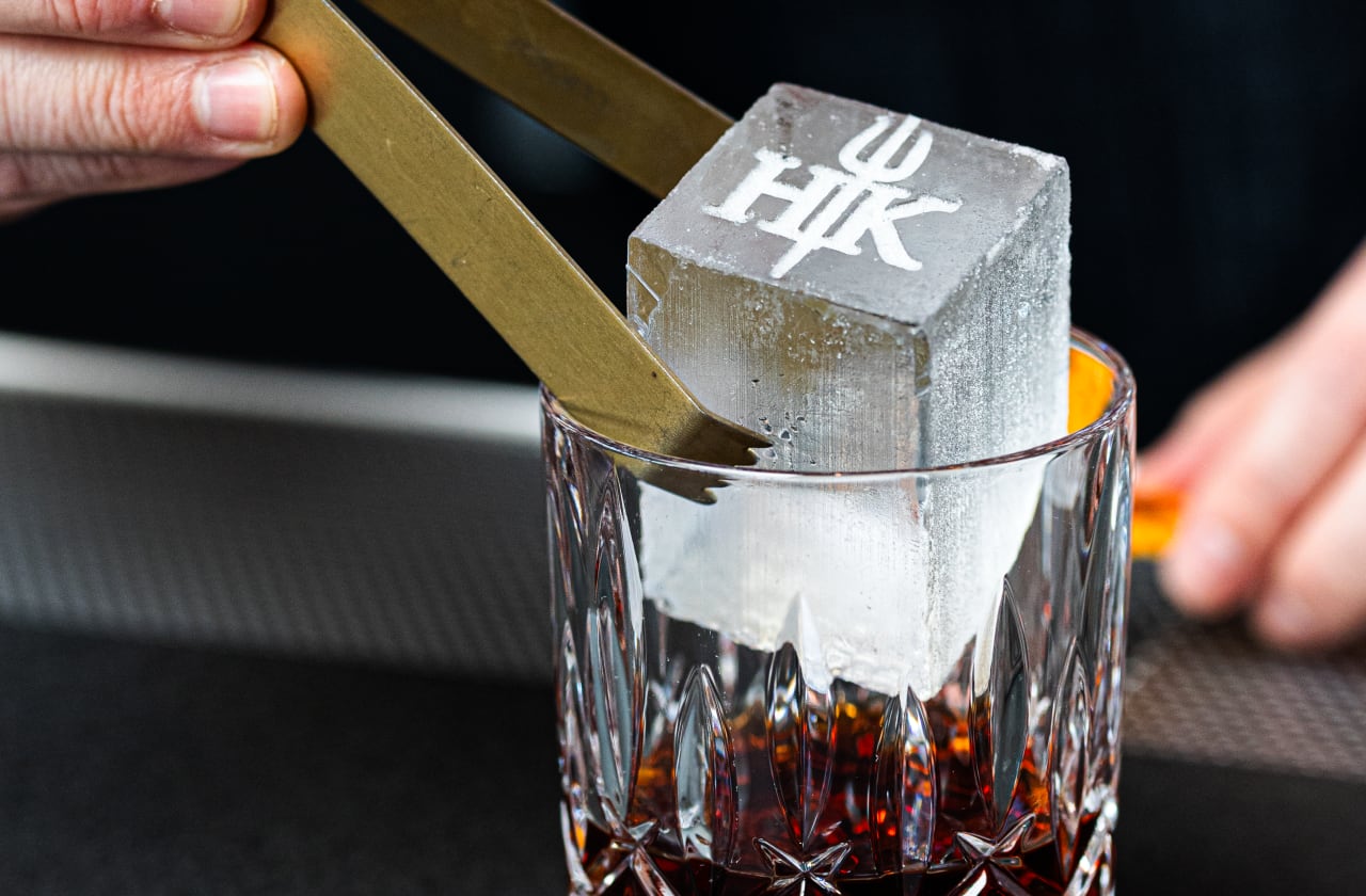 A cube of ice with the Hell's Kitchen logo etched into it, inside a glass.