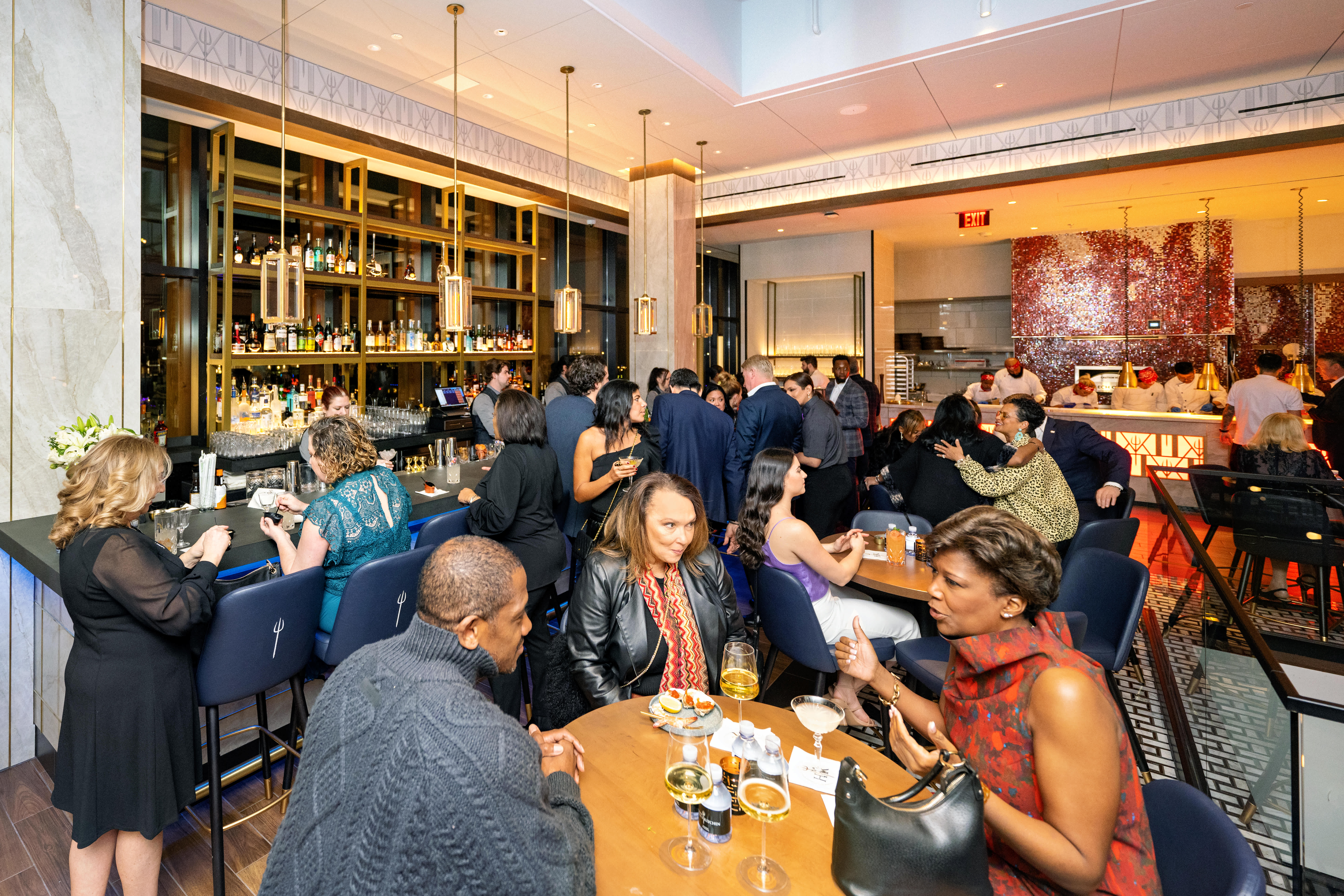 A large group of diners standing talking and also sitting at tables at Hell's Kitchen.