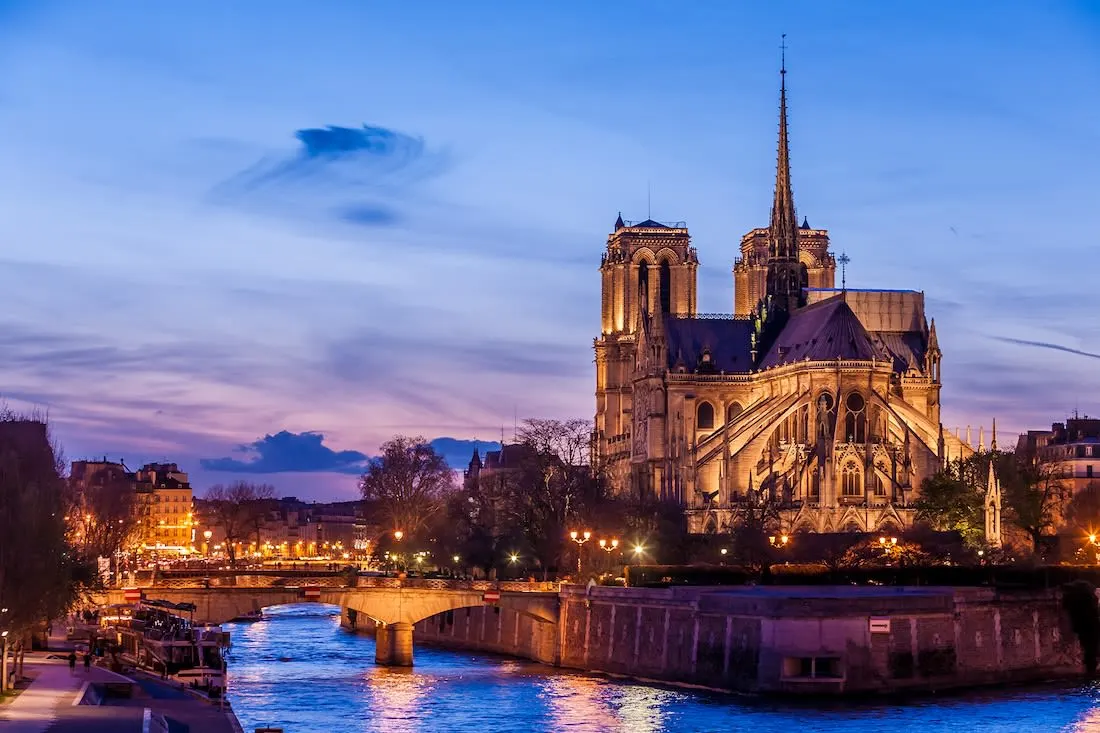 The Lit exterior of the back of Notre Dame Cathedral with an evening sky behind