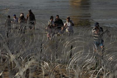 Three migrants who had managed to evade National Guard and cross the Rio  Grande onto U.S. territory wait for Border Patrol along a wall set back  from the geographical border, in El