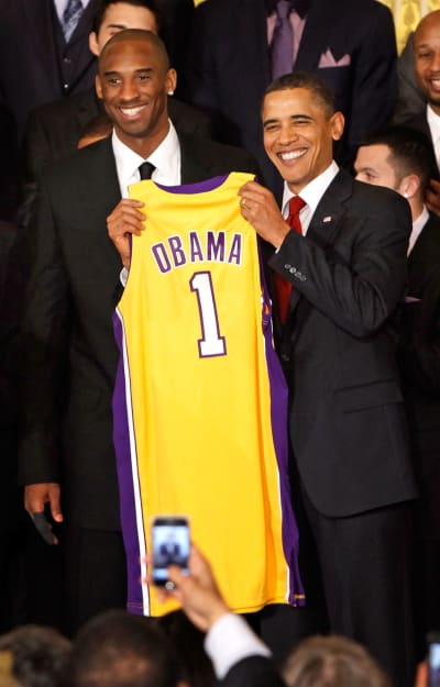 Kobe Bryant smiles and poses with a basketball wearing Laker home color  shoes and jersey at