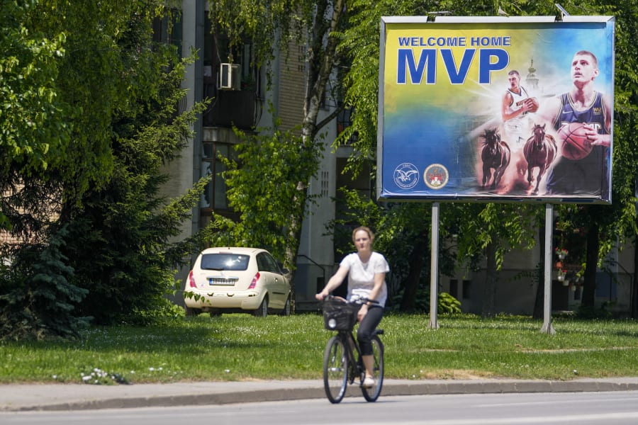 A woman rides a bicycle past a billboard showing Denver Nuggets center Nikola Jokic in the northern Serbian town of Sombor, Sunday, June 18, 2023. Jokic came to Serbia after the Denver Nuggets won the NBA Championship with a victory over the Miami Heat in Game 5 of basketball's NBA Finals. (AP Photo/Darko Vojinovic)