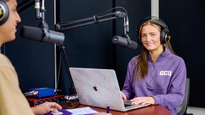 GCU student sitting at table with headphones and computer recording a podcast