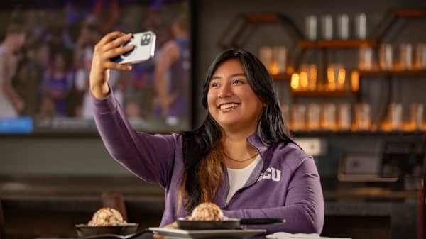 Student wearing GCU jacket sitting in restaurant taking a selfie