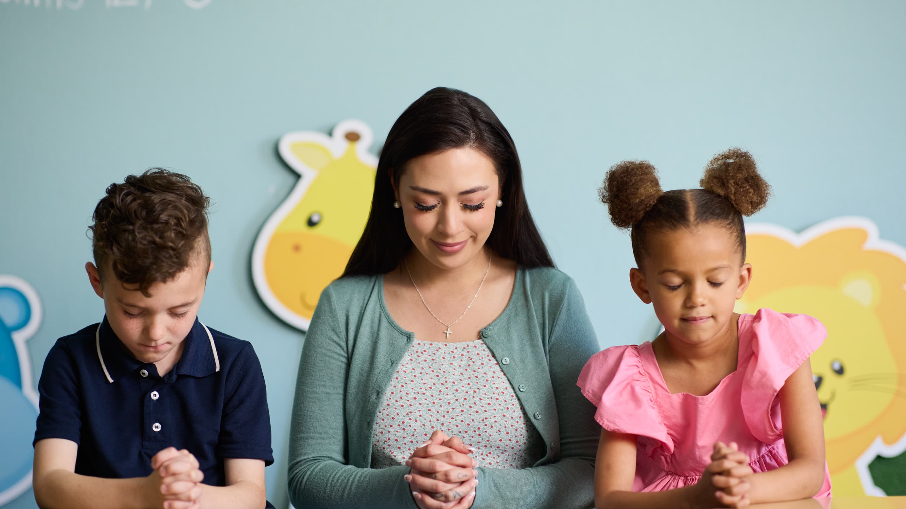 Female youth ministry degree student praying with young kids in classroom