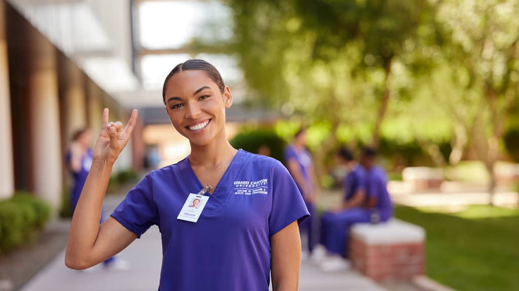 GCU MSN Student Smiles in Scrubs with "Lopes Up" Symbol