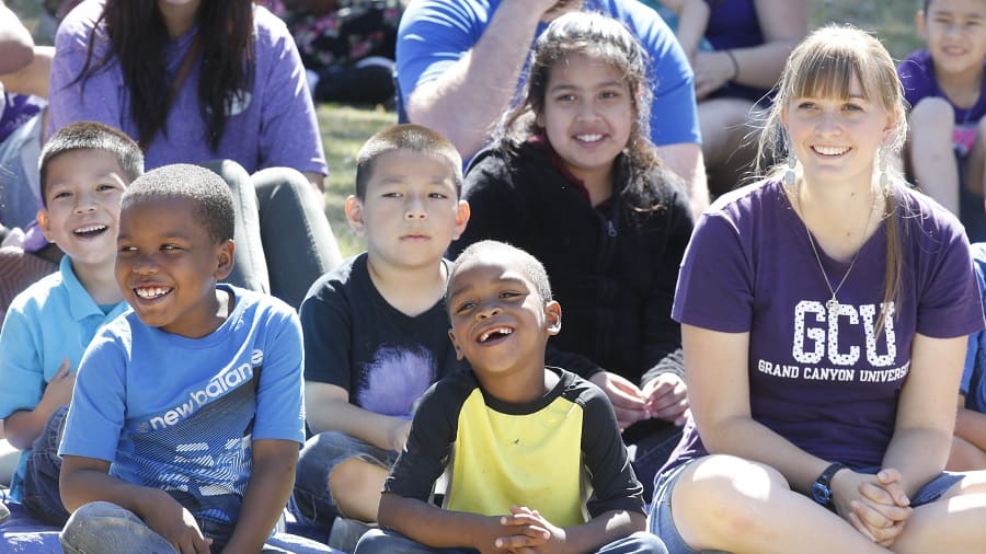 Young children sitting on the ground with GCU student volunteer