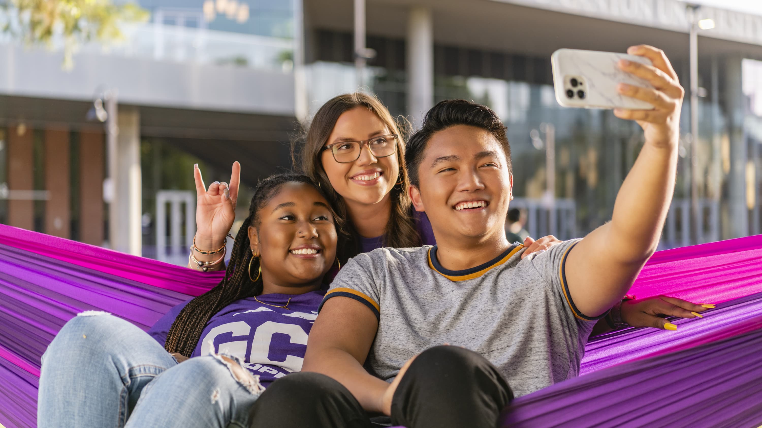 Male and female GCU students taking selfie while sitting in hammock on campus