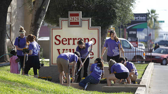 Group of GCU students in purple shirts planting flowers in front of a sign in the community
