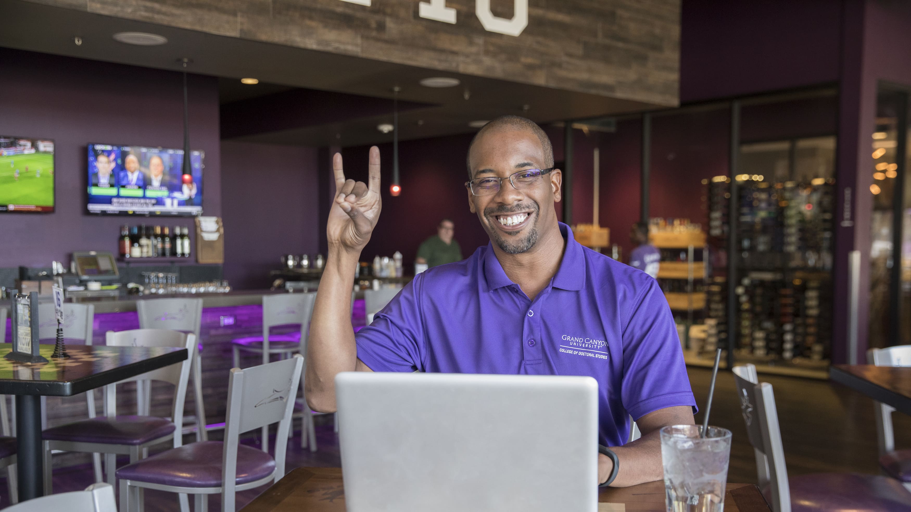 Male DBA degree student smiling with Lopes Up hand sign while working online