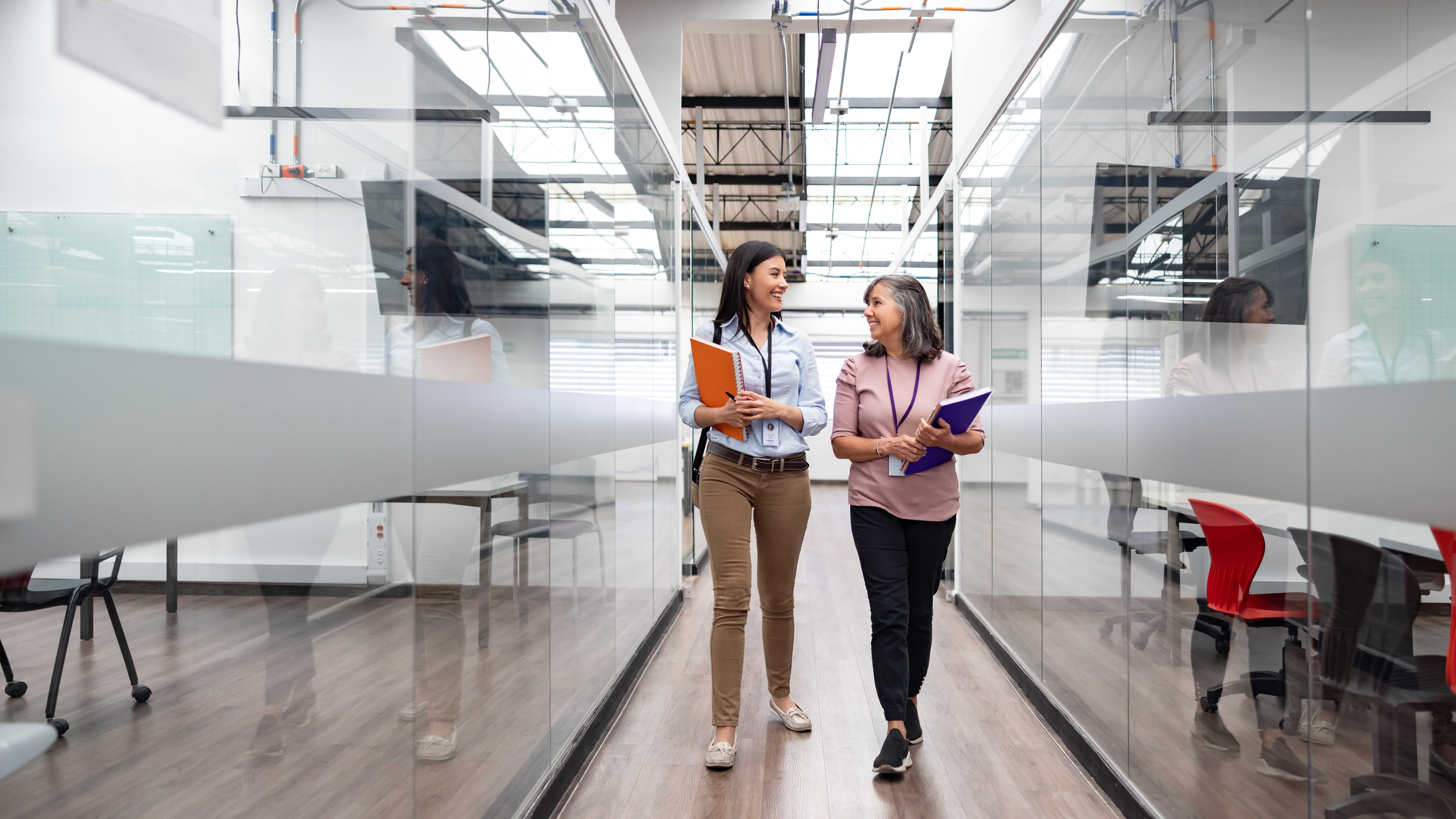 Two Communication Workers Walk Through Office Hall After Earning Communication Degrees From GCU