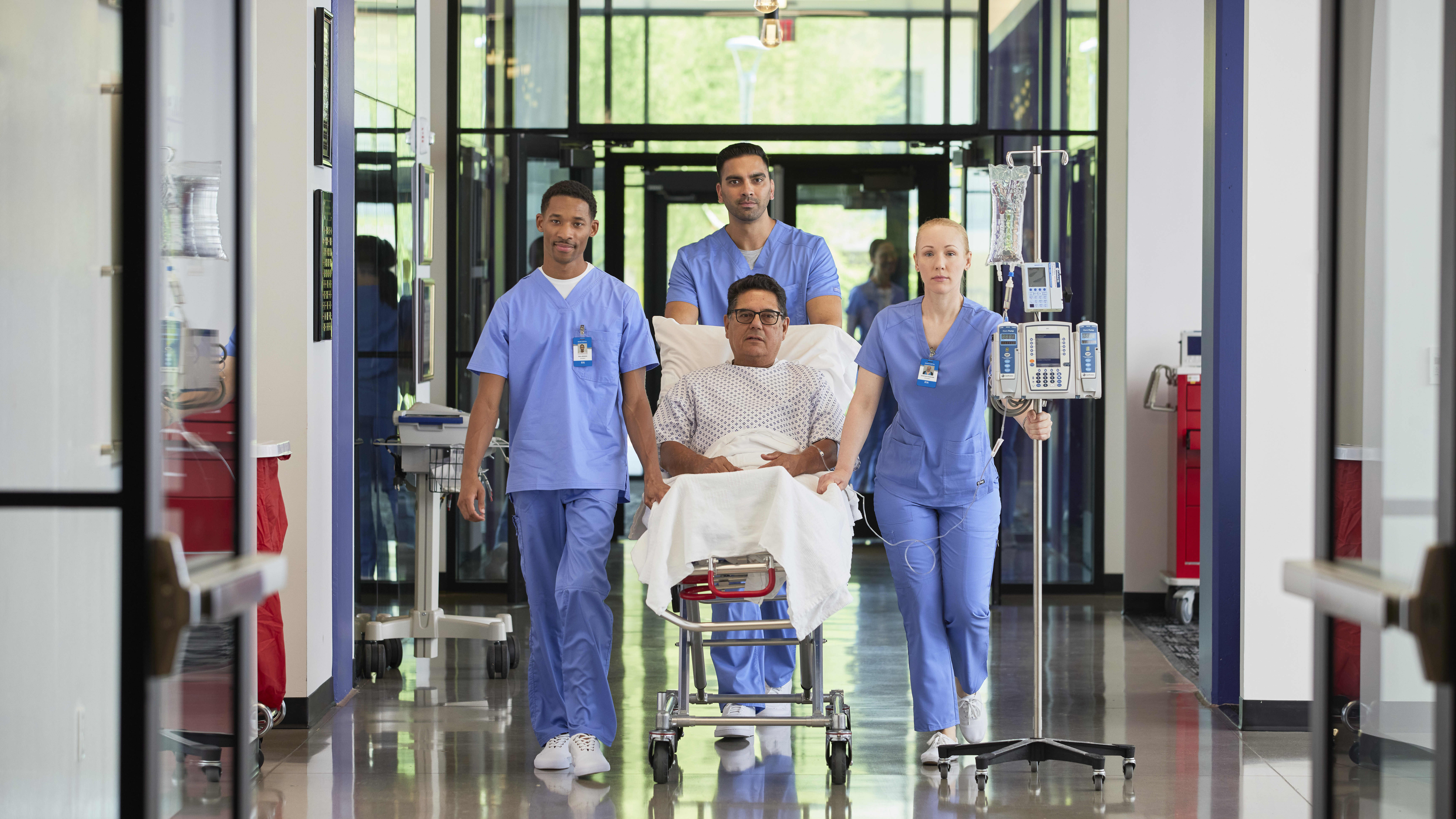 Group of male and female nurses in hospital hallway with patient on bed