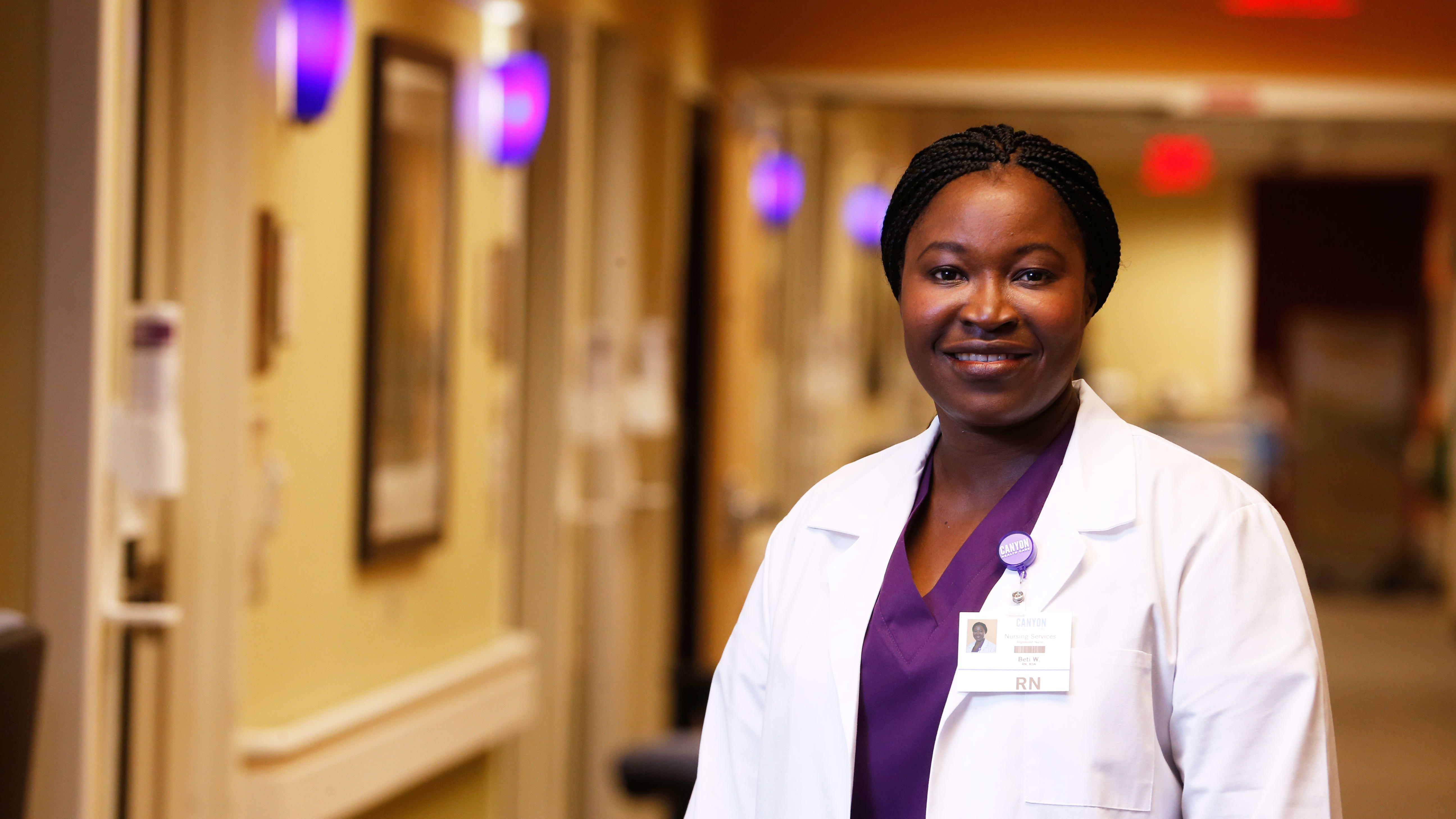 Female DNP degree student at GCU smiling in white lab coat in hospital hallway