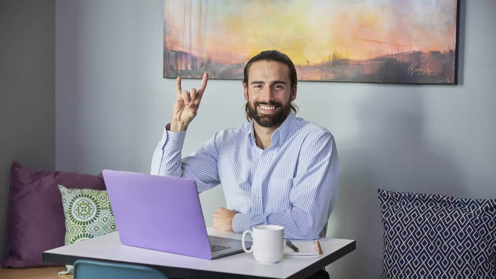 Human Resource Employee Smiles at Camera Working from Laptop After Earning MBA From GCU