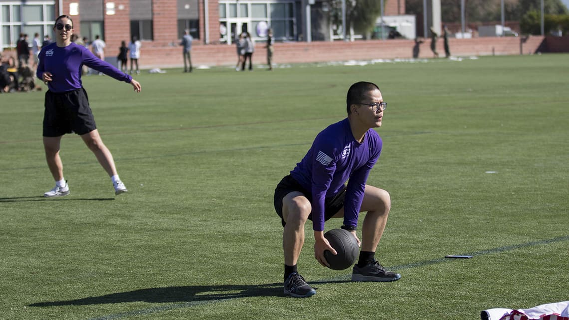 ROTC PT day with student squatting to throw a heavy medicine ball