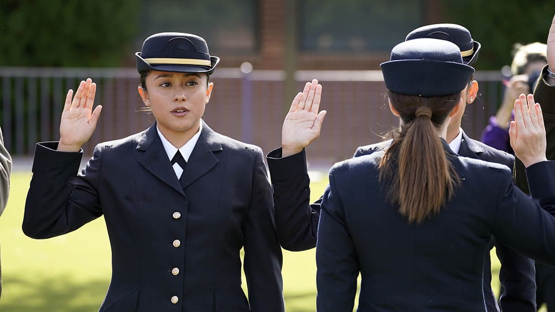 Female cadets in dress blues raise hands to be sworn in at the ROTC Commissioning Ceremony