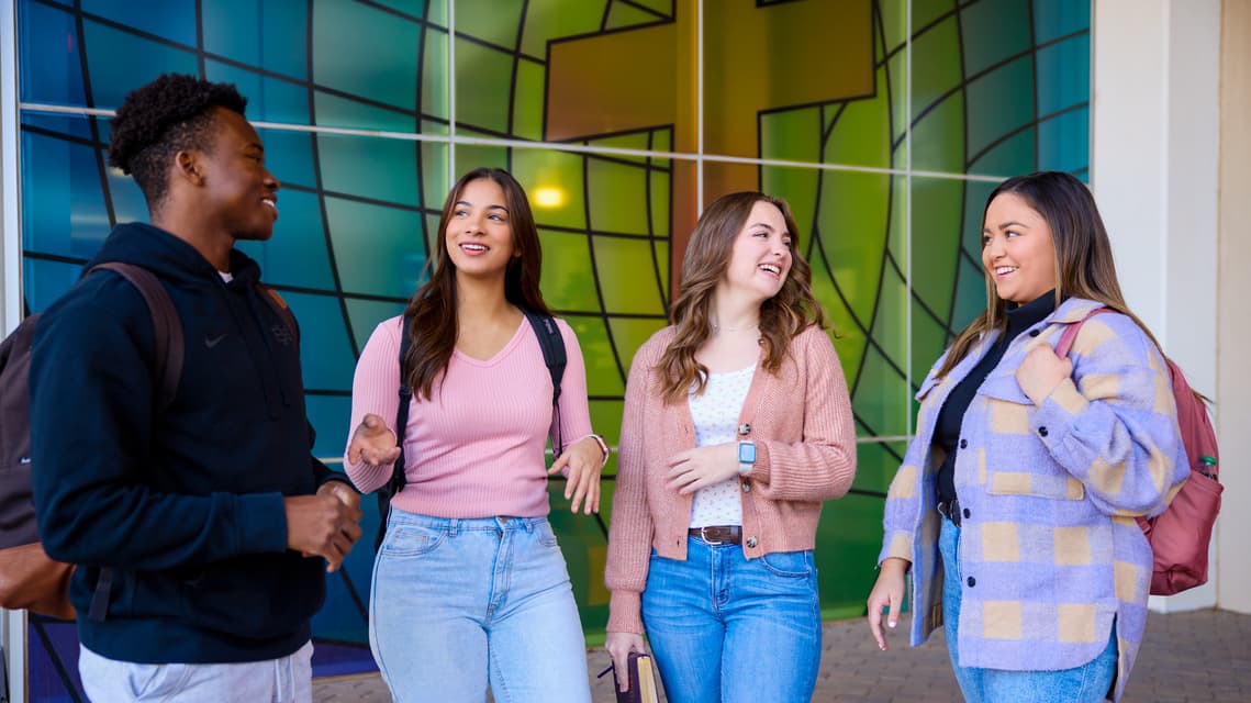 Group of grand canyon students stand talking near stained glass