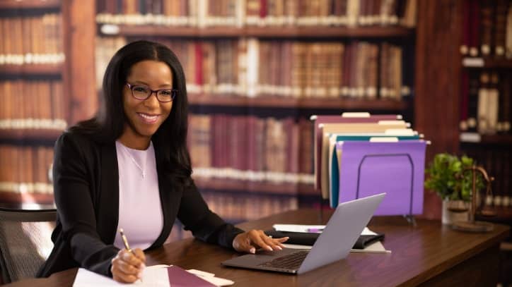 MPA student smiling while working on computer and writing on paper