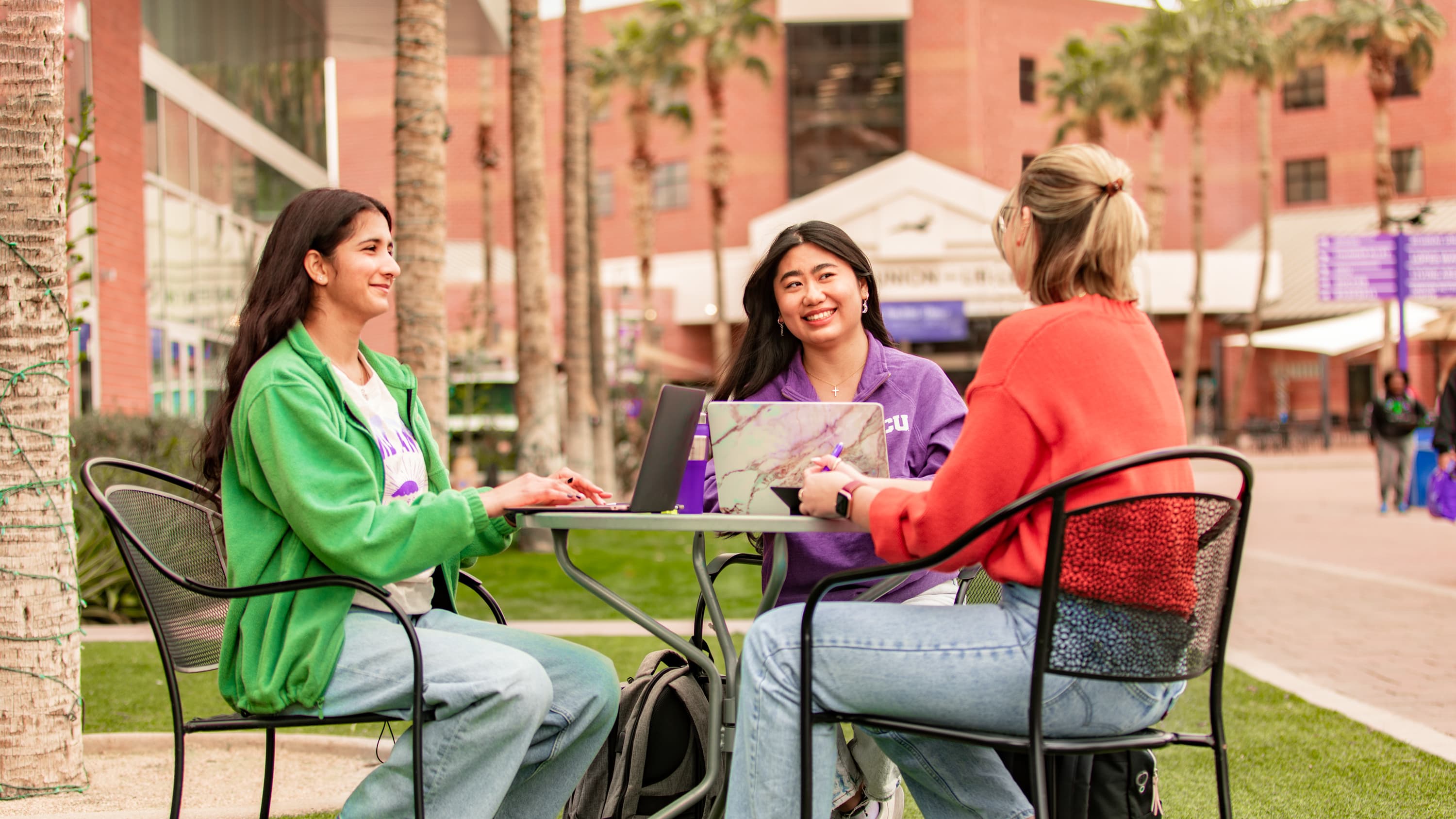 Three female psychology certificate students working outside on laptops